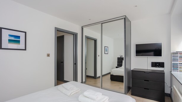 Et moderne hotelværelse med seng, stort spejl, fjernsyn og garderobeskab.