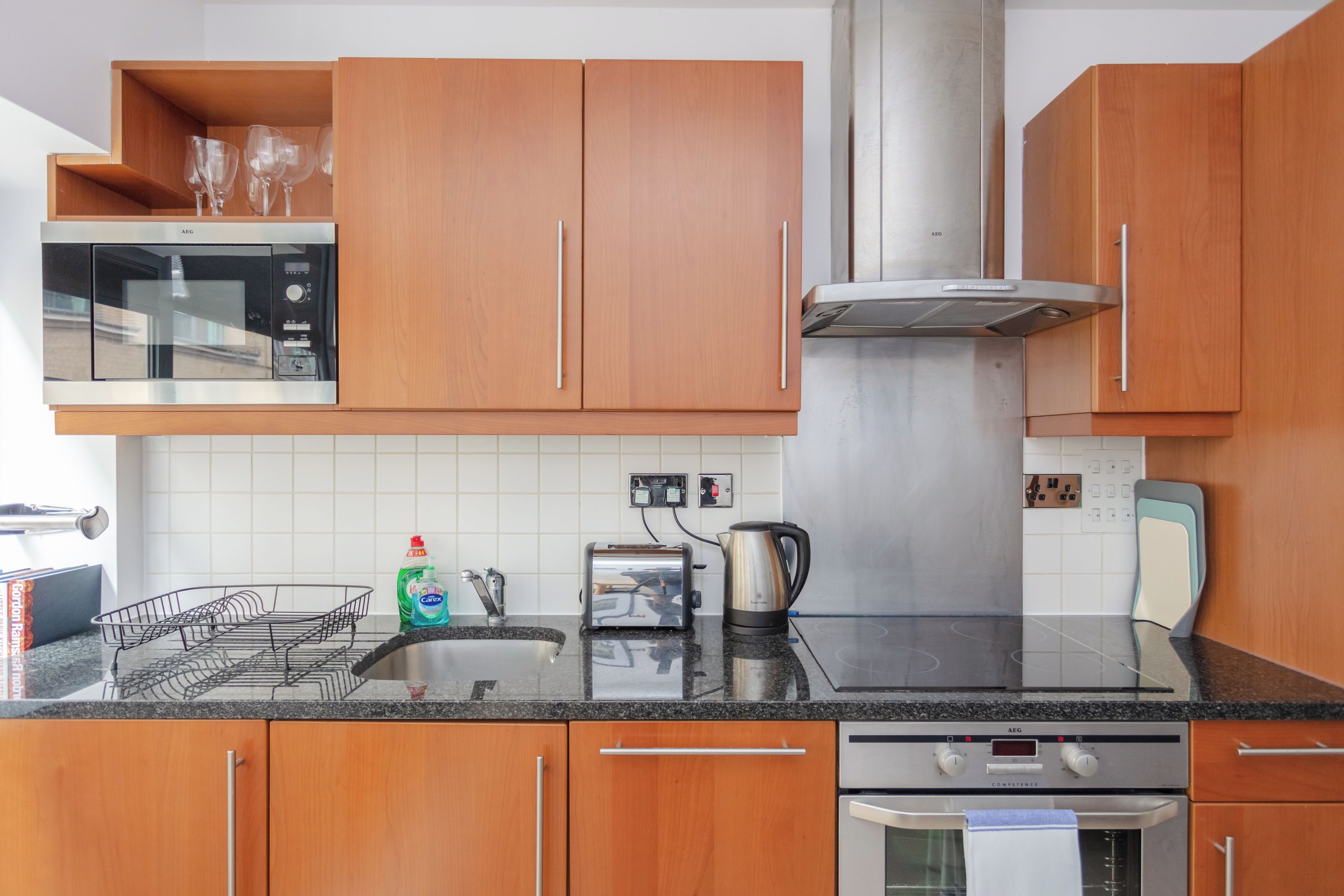 Una cocina moderna con armarios de madera, un microondas de acero inoxidable, un tostador y una tetera sobre la encimera.
