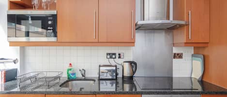 Une cuisine moderne avec des meubles en bois, un four à micro-ondes en acier inoxydable, un grille-pain et une bouilloire posés sur le plan de travail.
