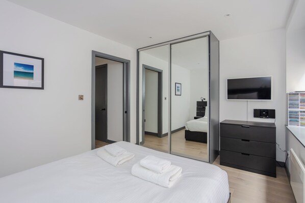 A modern hotel room with a bed, a TV, a wardrobe, and a mirror.