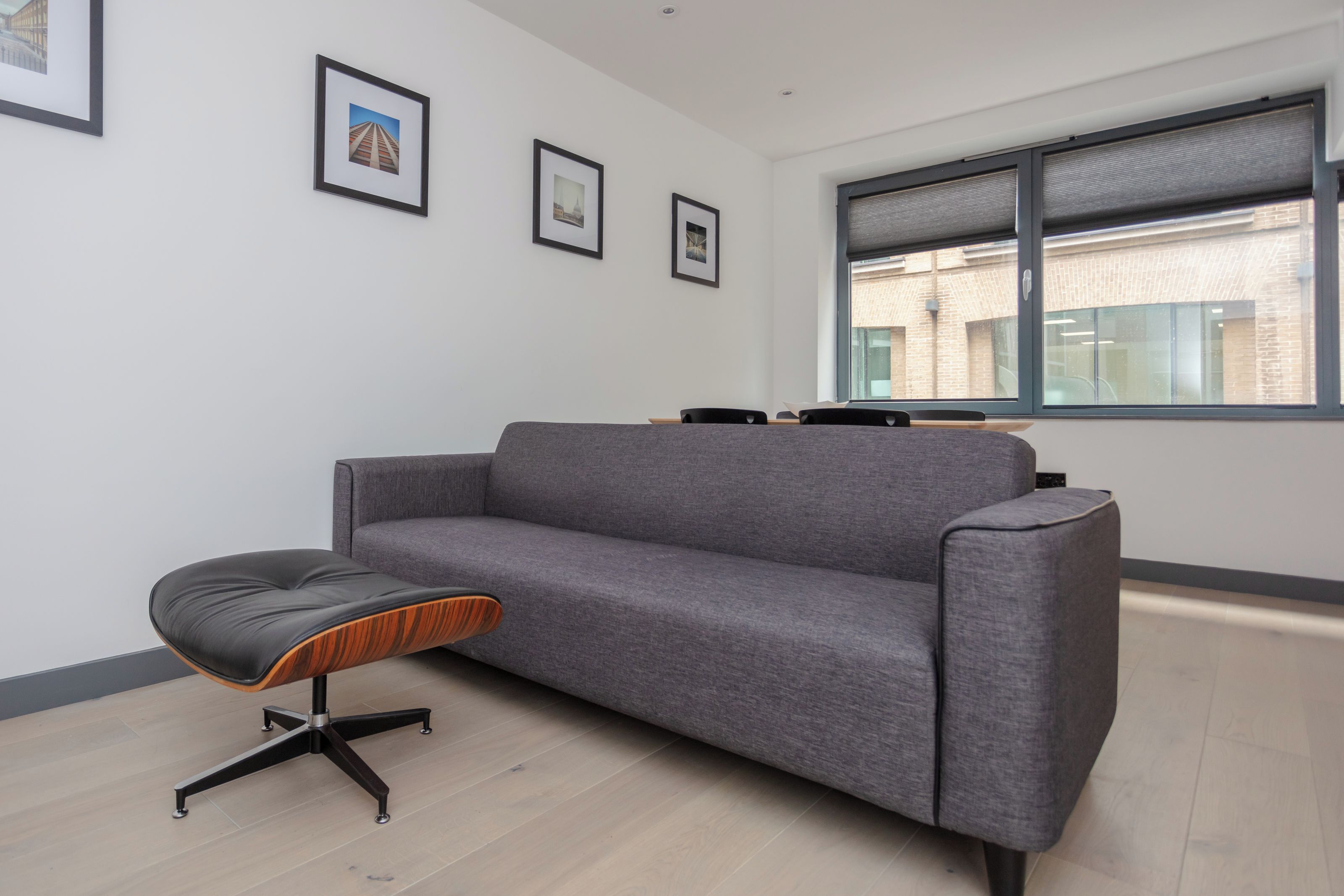 A modern office space with a grey sofa, a black and wooden stool, and framed pictures on the wall.