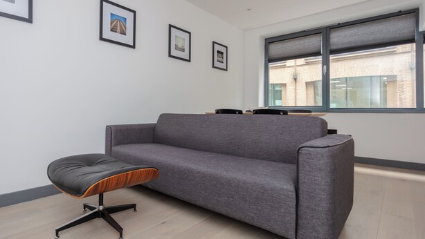 A modern office space with a grey sofa, a black and wooden stool, and framed pictures on the wall. - Centrally Located 1BD Flat in the Heart of London (London)