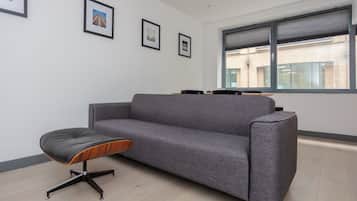 A modern office space with a grey sofa, a black and wooden stool, and framed pictures on the wall.