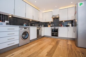 Una cocina moderna con armarios blancos, lavadora Bosch, lavavajillas y refrigerador.