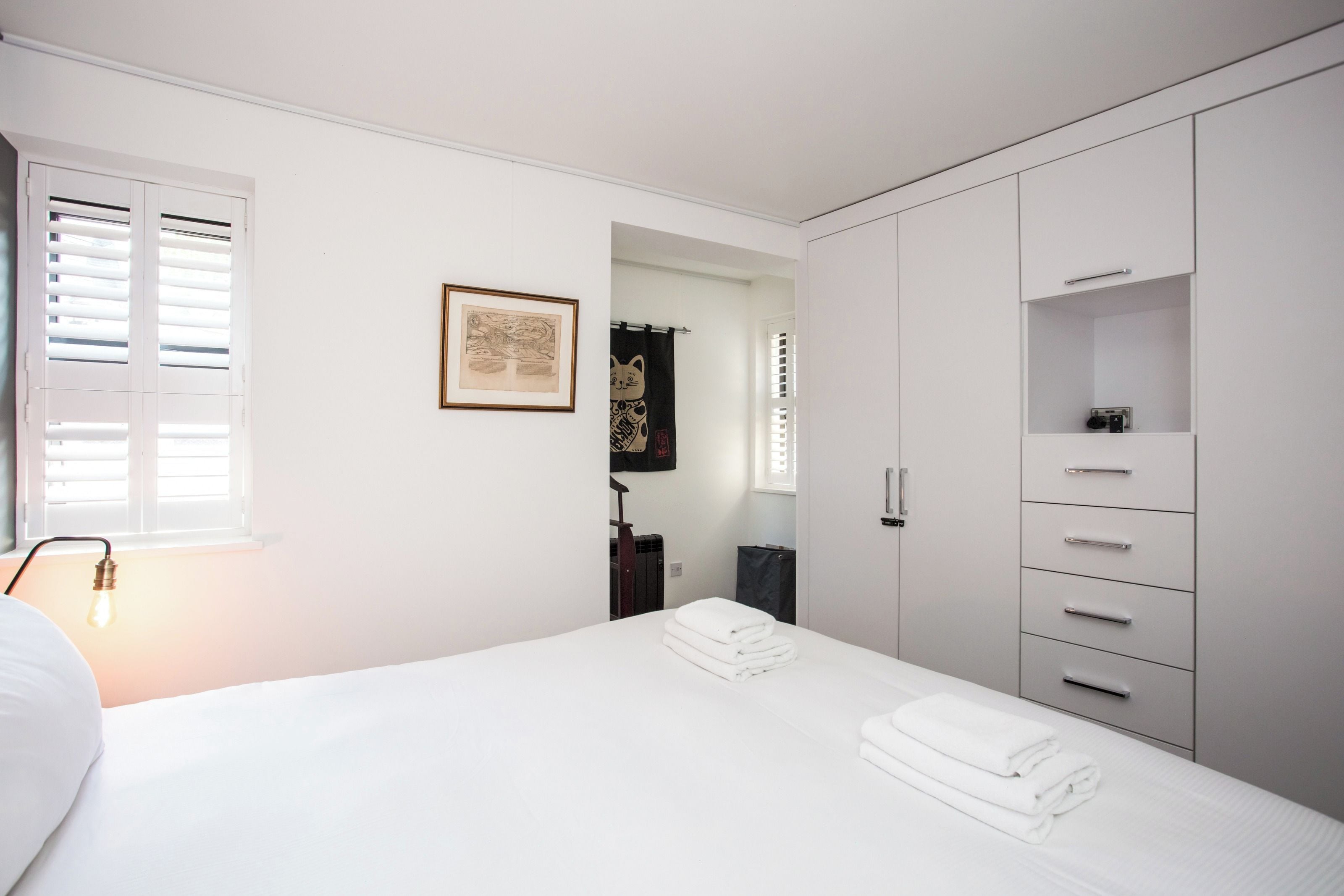 A bedroom with a bed, a wardrobe, a framed map, and a window with blinds.