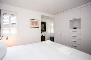 A bedroom with a bed, a wardrobe, a framed picture, and a window with blinds.