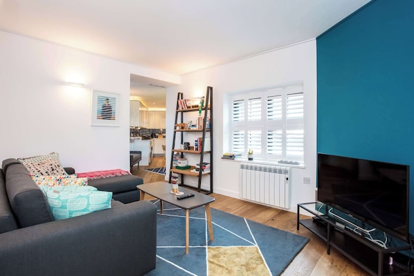 A modern living room with a sofa, coffee table, TV, bookshelf, and a window with blinds.