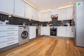 A modern kitchen with white cabinets, a washing machine, a dishwasher, and a refrigerator.