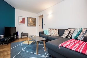 A modern living room with a grey sofa, colorful pillows, a coffee table, a TV, and a wall-mounted map.