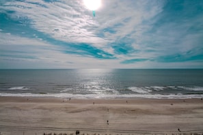 A beach with a clear sky, calm sea, and a few people walking.