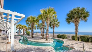 A swimming pool with a curved design, surrounded by palm trees and a white pergola. - 2BD Ocean View-Lazy River/Hot Tubs/Indoor Pool (North Myrtle Beach)
