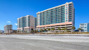 Ett hotell vid stranden med flera våningar, ett parkeringsgarage och en sandstrand i förgrunden.