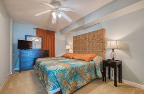 A bedroom with a bed, a dresser, a television, and a ceiling fan.