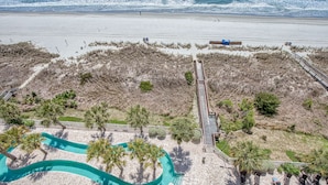 Ein Resort direkt am Strand mit Swimmingpool, Palmen und einer Promenade, die zum Strand führt.