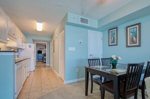 A kitchen with white cabinets, a refrigerator, and a dining area with a table and chairs.