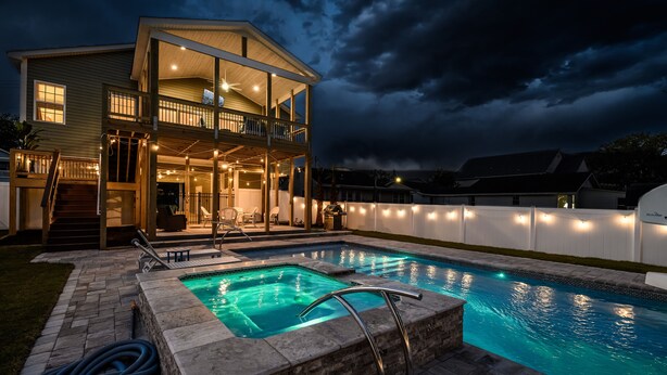 Una casa de dos pisos con piscina, terraza cubierta e interior bien iluminado.