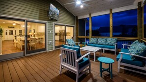 Un patio al aire libre cubierto, con suelo de madera, muebles blancos y cojines turquesa.