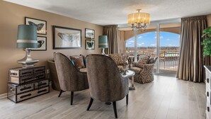 A spacious living room with a large window, two patterned armchairs, a small table, and a decorative lamp. - Spectacular 3BD Corner Unit - Waterway Views - Large Square Footage (North Myrtle Beach)