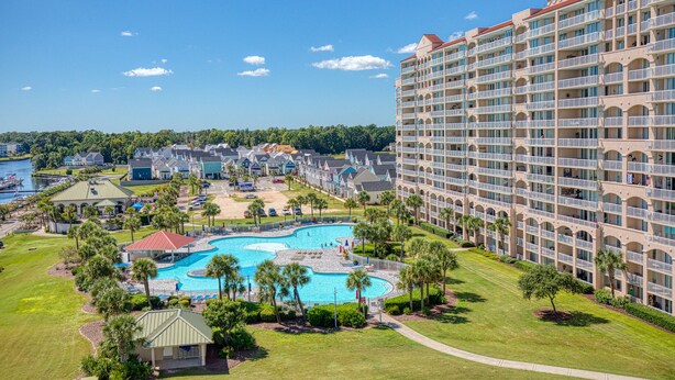 A large hotel with multiple balconies and a central swimming pool surrounded by palm trees and a well-maintained lawn. - Spectacular 3BD Corner Unit - Waterway Views - Large Square Footage (North Myrtle Beach)