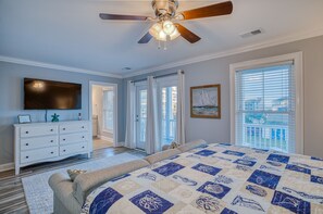 Une chambre à coucher comprenant un lit, un ventilateur de plafond, une télévision, une commode et une fenêtre avec des stores.