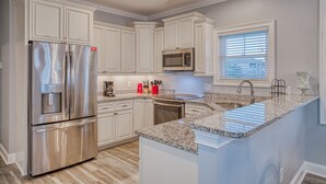 Una cocina moderna con armarios blancos, electrodomésticos de acero inoxidable, encimeras de granito y una isla integrada con pileta.