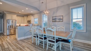 Una cocina amplia con muebles blancos, una isla central y un comedor con sillas blancas y una mesa de madera.