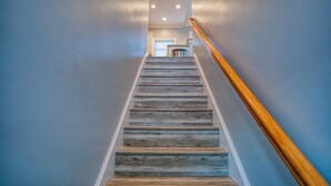 Una escalera de madera con escalones y barandilla, que conduce a un rellano con una puerta y un bote de basura.