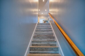 A staircase with wooden steps and a wooden handrail, leading to a landing with a door and a trash can.