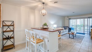 Een ruime woonkamer met een keukeneiland, witte meubels en een balkon met uitzicht.