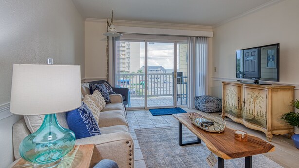 Een woonkamer met een bank, een salontafel, een televisie en een balkon met uitzicht op gebouwen.