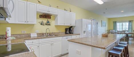 A kitchen with white cabinets, a granite countertop, and a central island with bar stools.