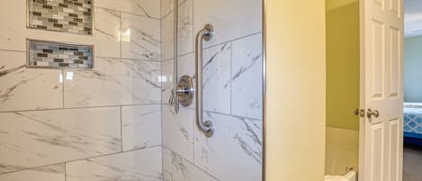 A bathroom with a walk-in shower, a handrail, and a tiled floor.