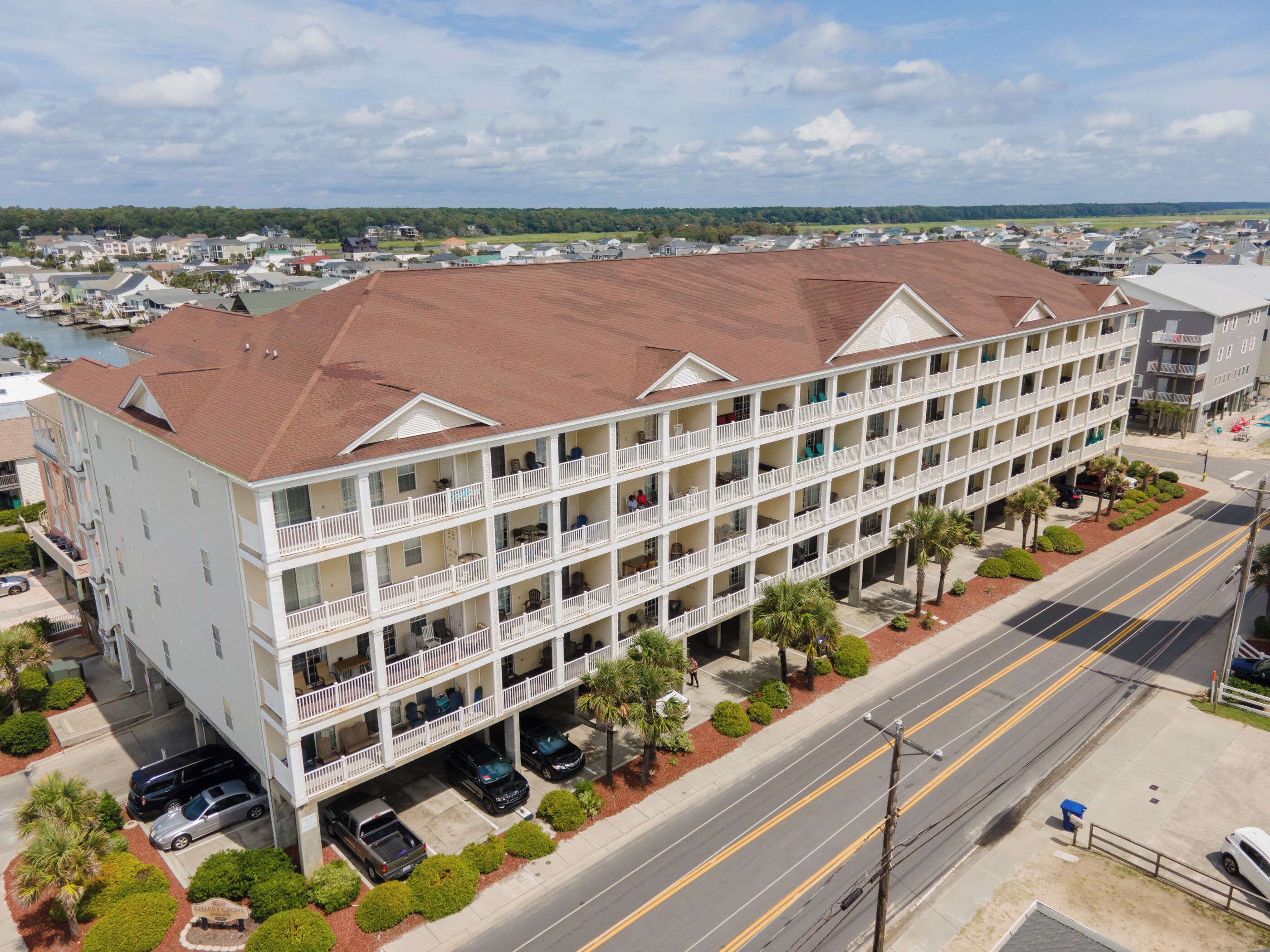 A multi-story hotel with balconies, a parking lot, and a view of a body of water.