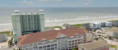 A hotel with multiple floors, a swimming pool, and a view of the beach and ocean.