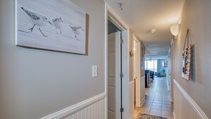 A hallway with a framed artwork of birds, a door leading to another room, and a patterned rug on the floor. - Beautiful Oceanfront-3BD-Pool/Hot Tub/Lazy River-Bahama Sands (North Myrtle Beach)
