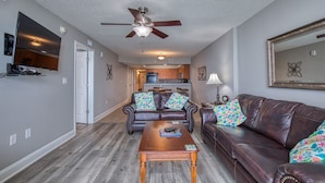 A living room with a brown leather sofa, a wooden coffee table, and a ceiling fan. - Beautiful Oceanfront-3BD-Pool/Hot Tub/Lazy River-Bahama Sands (North Myrtle Beach)
