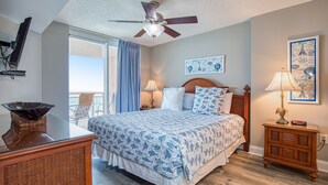 A bedroom with a bed, a nightstand, a chair, a ceiling fan, and a window with curtains. - Beautiful Oceanfront-3BD-Pool/Hot Tub/Lazy River-Bahama Sands (North Myrtle Beach)