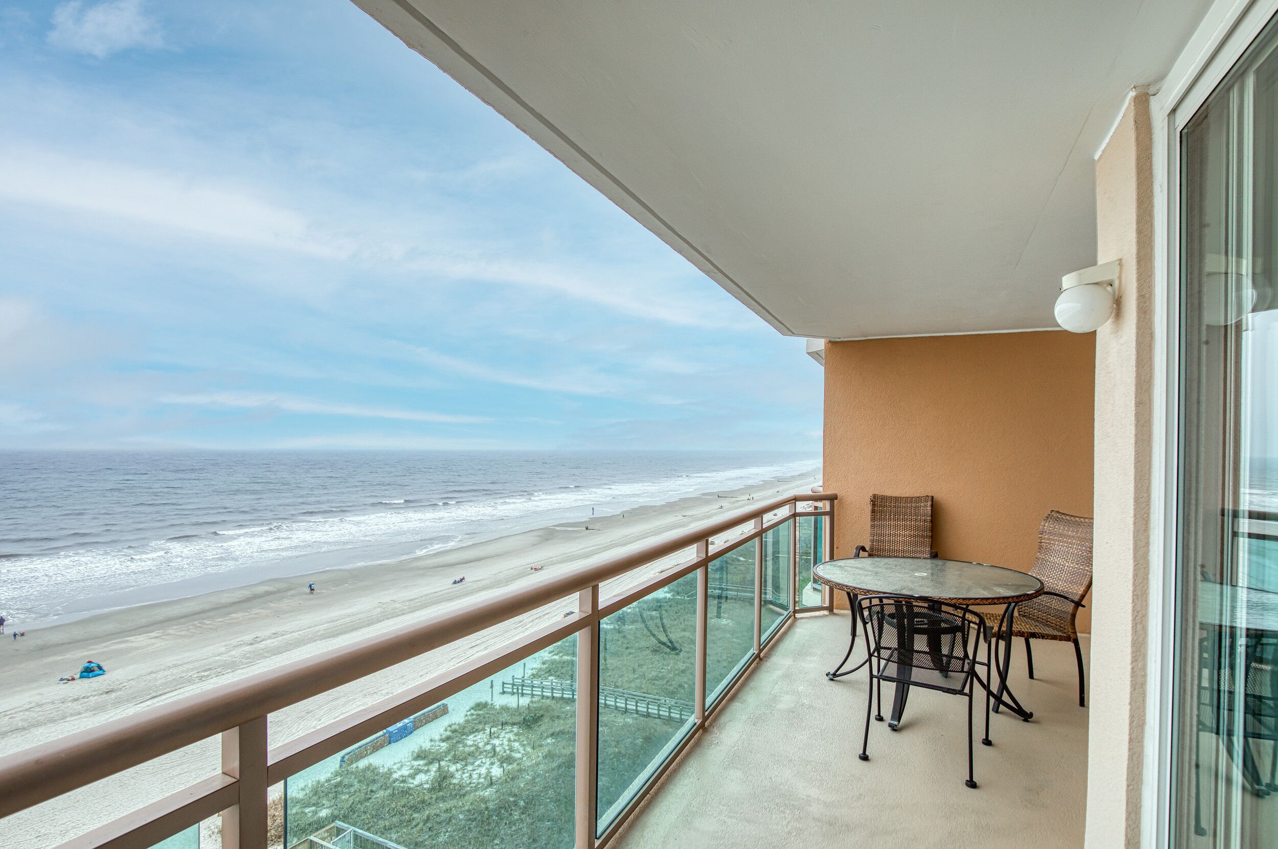 A balcony with a glass railing overlooking a beach.
