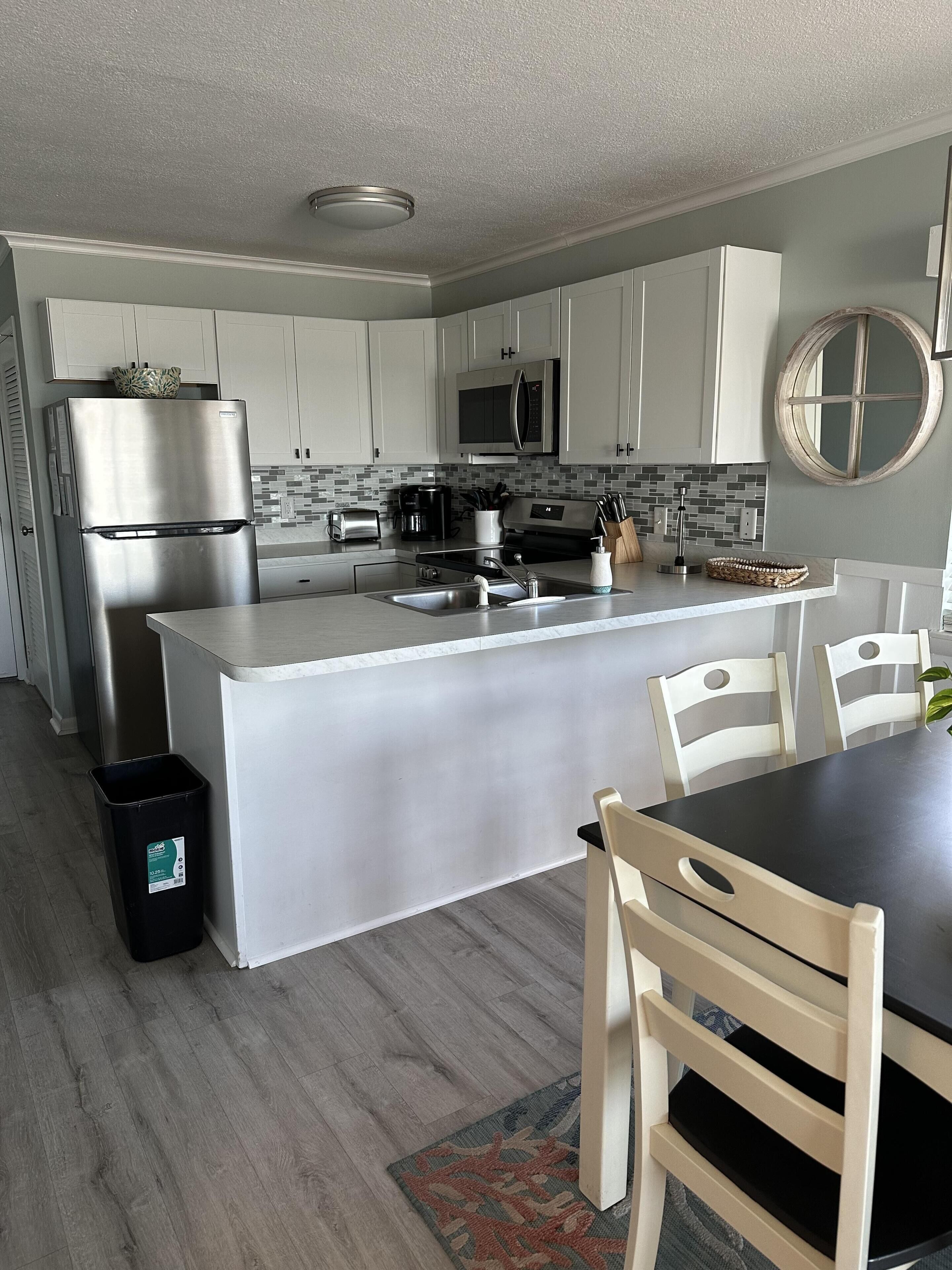 Una cocina moderna con armarios blancos, electrodomésticos de acero inoxidable, una isla central y un comedor con sillas.