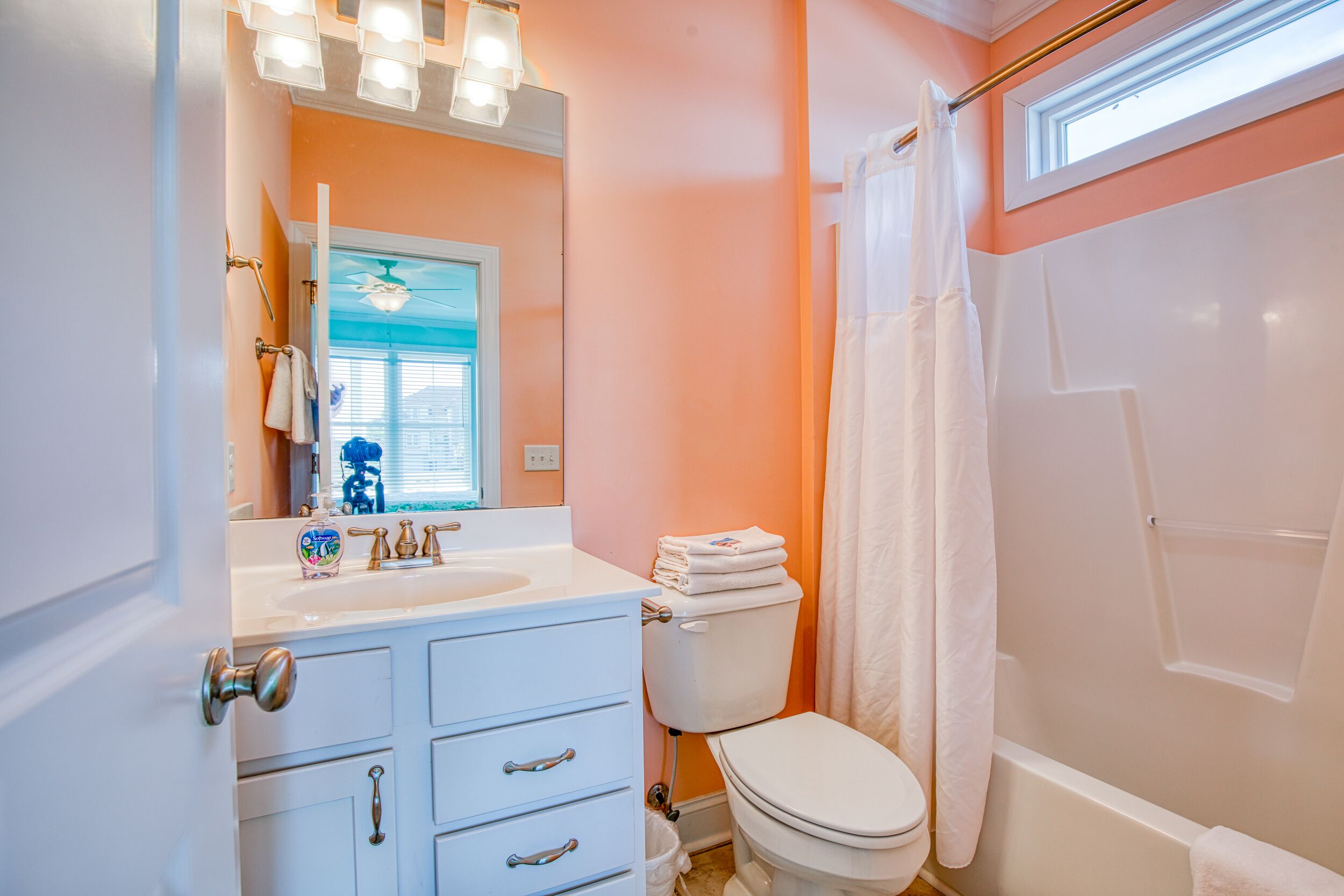 A bathroom with a white sink, vanity, and toilet. There is a window with a view of the outside, and a shower curtain.