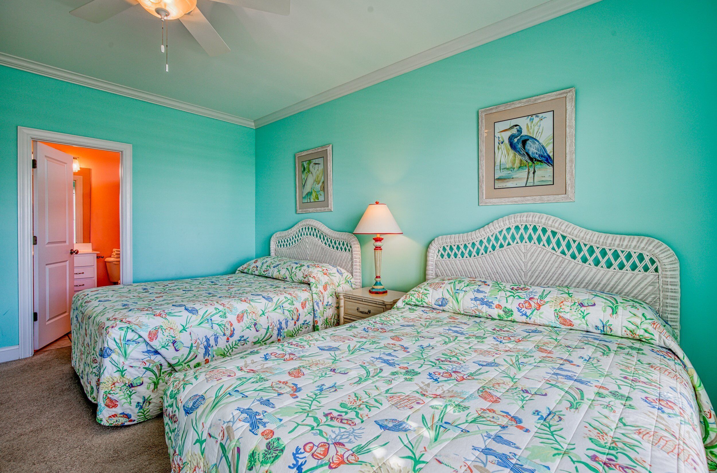 A bedroom with two beds, a nightstand, a lamp, and a ceiling fan.