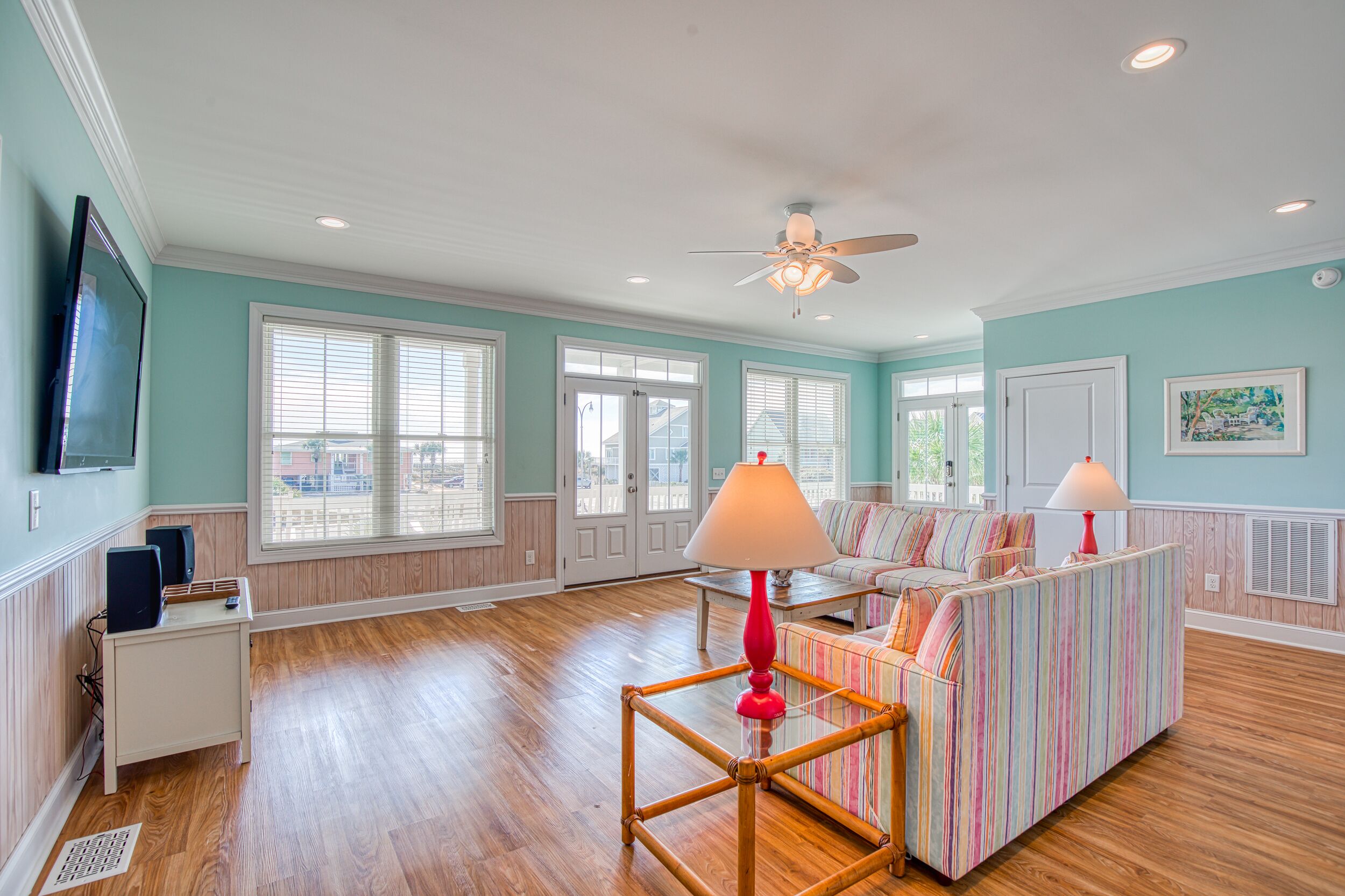 A spacious living room with a large window, a ceiling fan, and a striped sofa.