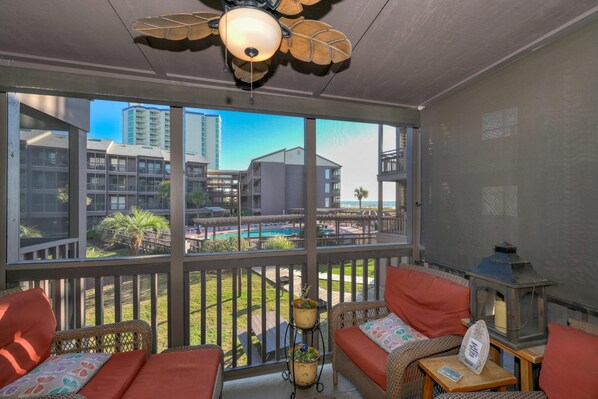 Enjoy the serene view of the pool and surrounding buildings from this balcony, complete with a ceiling fan and comfortable seating area.