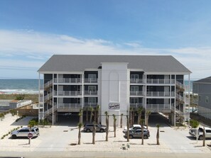 A multi-story hotel with balconies, a parking area, and a view of the beach. - Sea Oats D-3, 3BD 2BA Oceanfront Paradise (North Myrtle Beach)