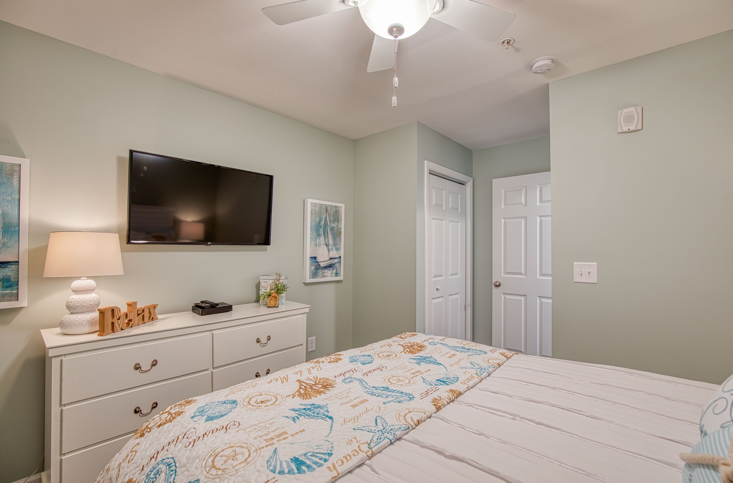 A bedroom with a bed, a dresser, a television, and a ceiling fan.