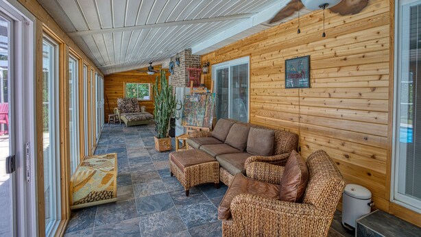 A log cabin interior with a wooden ceiling, a ceiling fan, a large window, a sofa, a coffee table, and a potted plant. - 4BD Beach House-Private Pool-3 Min Walk 2Beach (North Myrtle Beach)