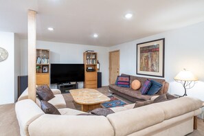 A modern living room with a sofa, coffee table, and TV. There are bookshelves and a painting on the walls.