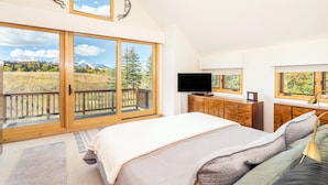 Un dormitorio con una cama grande, televisor, armarios de madera y un balcón con vistas a la montaña.