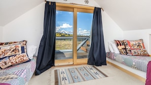 Un dormitorio con un amplio ventanal corredera que da a un balcón, dos camas con ropa de cama estampada y vistas a montañas.