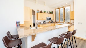 Una cocina moderna con una isla grande, taburetes de bar, armarios de madera y vistas al exterior.